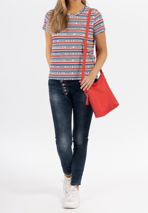 T-shirt a righe con testo rosso, bianco e blu, abbinato a jeans skinny scuri e una borsa a tracolla rossa. Scarpe da ginnastica bianche completano l'outfit.