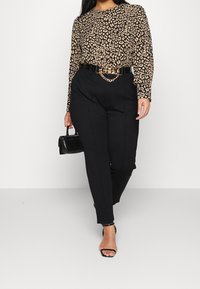 Un haut à manches longues imprimé léopard en beige et noir, associé à un pantalon noir ajusté. Les accessoires comprennent une ceinture en chaîne dorée et un petit sac à main noir.