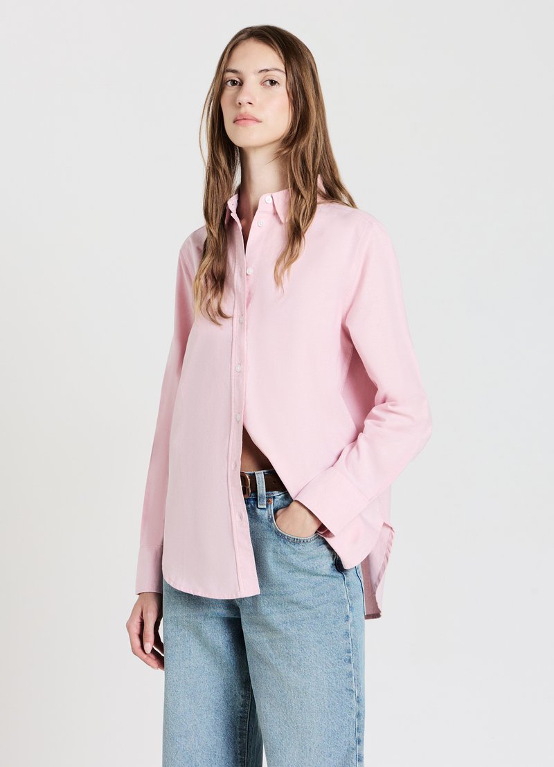 Light pink button-up shirt with long sleeves, a classic collar, and a relaxed fit, paired with high-waisted blue jeans.