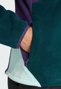 Fleece pullover in groen, paars en lichtblauw met een zak aan de zijkant, met een zachte textuur en contrasterende kleurpanelen.