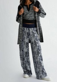 Felpa con zip nera e bianca, in tessuto texturizzato, abbinata a pantaloni larghi con stampa serpente blu, dotati di vita con cordino e sneakers bianche.