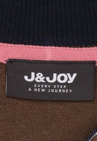 Encolure de sweater tricoté en marine, avec un accent côtelé rose et une étiquette texturée marron portant du texte blanc "J&JOY" et un slogan.