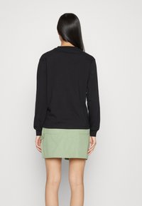Schwarzes Langarmshirt und hellgrüner Rock, beide aus weicher Baumwolle gefertigt. Das Oberteil hat ein einfaches Design mit einem runden Halsausschnitt und gerippten Bündchen.