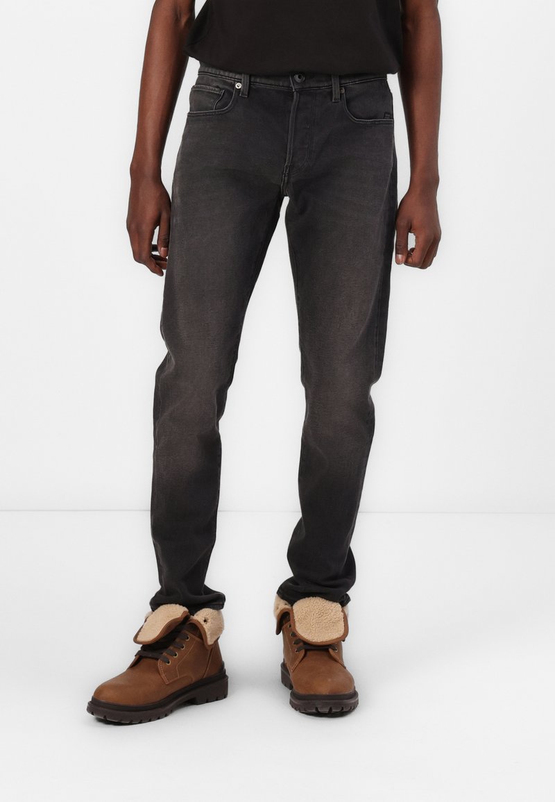 Jeans de mezclilla negra con un corte ajustado y un desvanecimiento sutil, combinados con botas de cuero marrón que tienen un collar forrado de piel y una suela resistente.