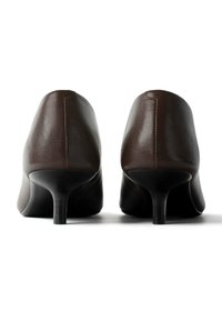 Paire de chaussures en cuir marron foncé à talon moyen, vues de dos, présentant un talon arrondi et une surface à texture lisse.