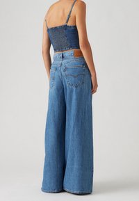 Ljusblå denimbyxor med vida ben och hög midja, med en bakre ficka, dubbla bakfickor och en fransad kant. Smockad denimkort topp.