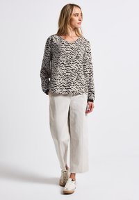 Maglia a maniche lunghe, scollo a V in beige con un motivo astratto nero, abbinata a pantaloni larghi color crema e sneakers chiare. Taglio semplice e rilassato.