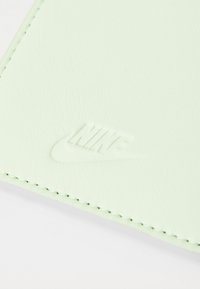 Mint green textured leather wallet with embossed Nike logo. Features white stitching along the edges, highlighting its design and craftsmanship.