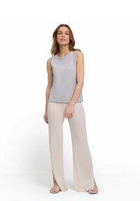 Top senza maniche grigio chiaro con scollo rotondo, abbinato a pantaloni beige a gamba larga con texture a coste e spacchi laterali.