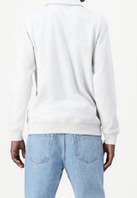 Sudadera de color gris claro con cuello, puños y dobladillo acanalados. Se combina con unos pantalones vaqueros de mezclilla light blue de cintura alta con bolsillos traseros.