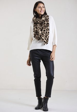 Cremfarbener Oversized-Pullover, Leopardenmuster-Schal, schwarze Fake-Leder-Hosen und schwarze Knöchelstiefel. Glatte Textur und lässige Passform.
