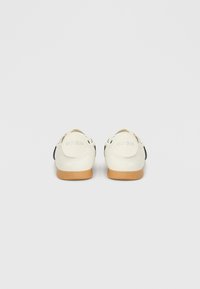 Ζευγάρι λευκών αθλητικών παπουτσιών Adidas με σόλες από καουτσούκ, εμφανιζόμενα από πίσω σε απλό ανοιχτό γκρι φόντο.