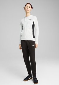 Vit zip-up hoodie med svarta detaljer, i kombination med svarta sweatpants med en logo, och svarta sneakers med brun sula.
