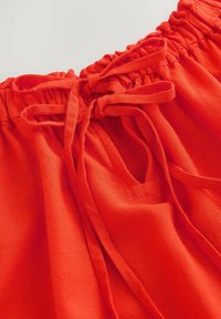 Rode stof met een geplooide taille, voorzien van strikken en een kleine uitsnijding. Gelaagde oppervlakte, lichtgewicht ontwerp geschikt voor casual gebruik.