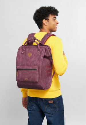 Sac à dos texturé violet avec deux poignées de transport, bretelles rembourrées, poche zippée à l'avant et détail de logo discret.