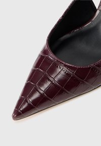 Burgundy pointed-toe pump with a glossy croc-embossed texture, black interior, and a sleek silhouette, featuring a slim, textured heel.