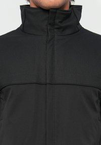Black softshell jacket with a high collar, smooth texture, and contrasting seam details. Features a minimalist design suitable for various activities.