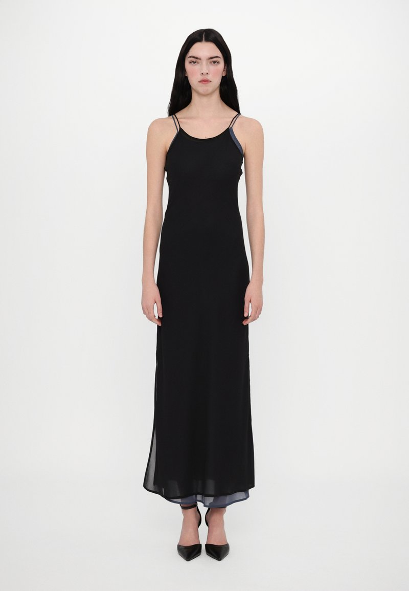 Rochie maxi fără mâneci, de culoare neagră, cu bretele subțiri, dintr-un material neted și cu fante laterale. Accentuata cu detalii suprapuse din material transparent la tiv.