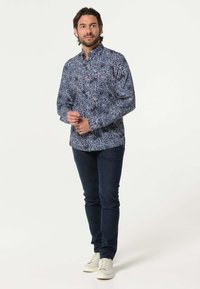 Navyblauw overhemd met lange mouwen met een bloemenpatroon in wit en lichtblauw, gecombineerd met donkere spijkerbroek en witte sneakers.