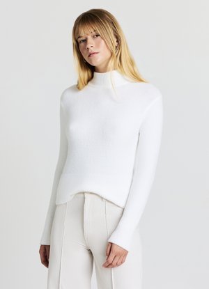 Weißer, gerippter Rollkragenpullover aus weichem, strukturiertem Strick. Mit langen Ärmeln und einem etwas längeren rückwärtigen Saum. Kombiniert mit hellen, gerippten Hosen.