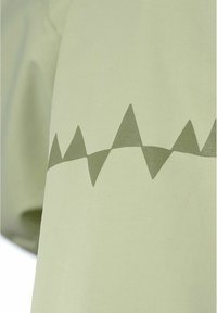 Vaaleanvihreä kangas, jonka pinnalla kulkee vaakasuora rivi tummanvihreitä kolmionmuotoisia huippuja.