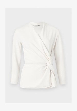 Λευκό μπλούζα με μακριά μανίκια, τύπου wrap, με V-λαιμόκοψη και λεπτομέρεια κόμπου στο πλάι, σε εφαρμοστή γραμμή, εμφανιζόμενη σε απλό ανοιχτό γκρι φόντο.