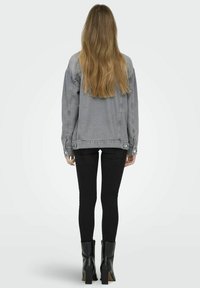 Giacca di jeans grigia con vestibilità comoda, abbinata a jeans skinny neri e stivaletti neri con tacco alto. Capelli lunghi e lisci visibili.