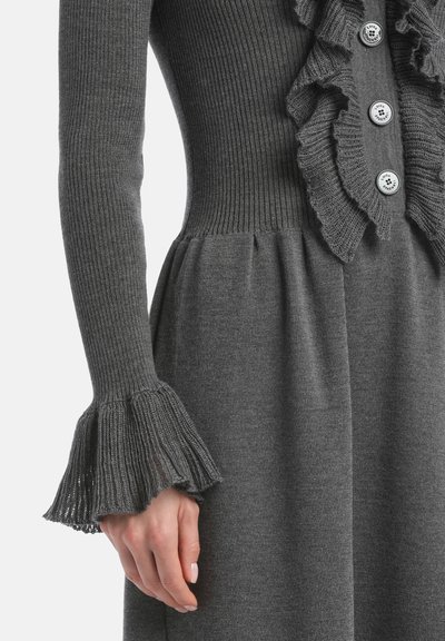 Abito grigio lavorato a maglia con texture a costine, davanti arricciato e polsini a campana. Presenta dettagli di bottoni lungo il corpetto per un tocco di interesse.