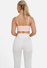 Svetloružový crop top s tenkými ramienkami, kombinovaný s bielymi legínami s vysokým pásom, ktoré majú sieťové panely a textúrovaný povrch.