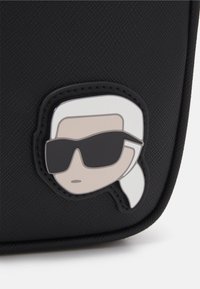Borsa nera testurizzata con un patch cartoon di una figura con capelli bianchi e occhiali da sole. Il patch è posizionato su una superficie liscia.