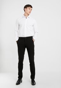 Vit långärmad skjorta i kombination med svarta slim-fit byxor. Skjortan har en diskret krage, och byxorna har en struktur med en slät finish.