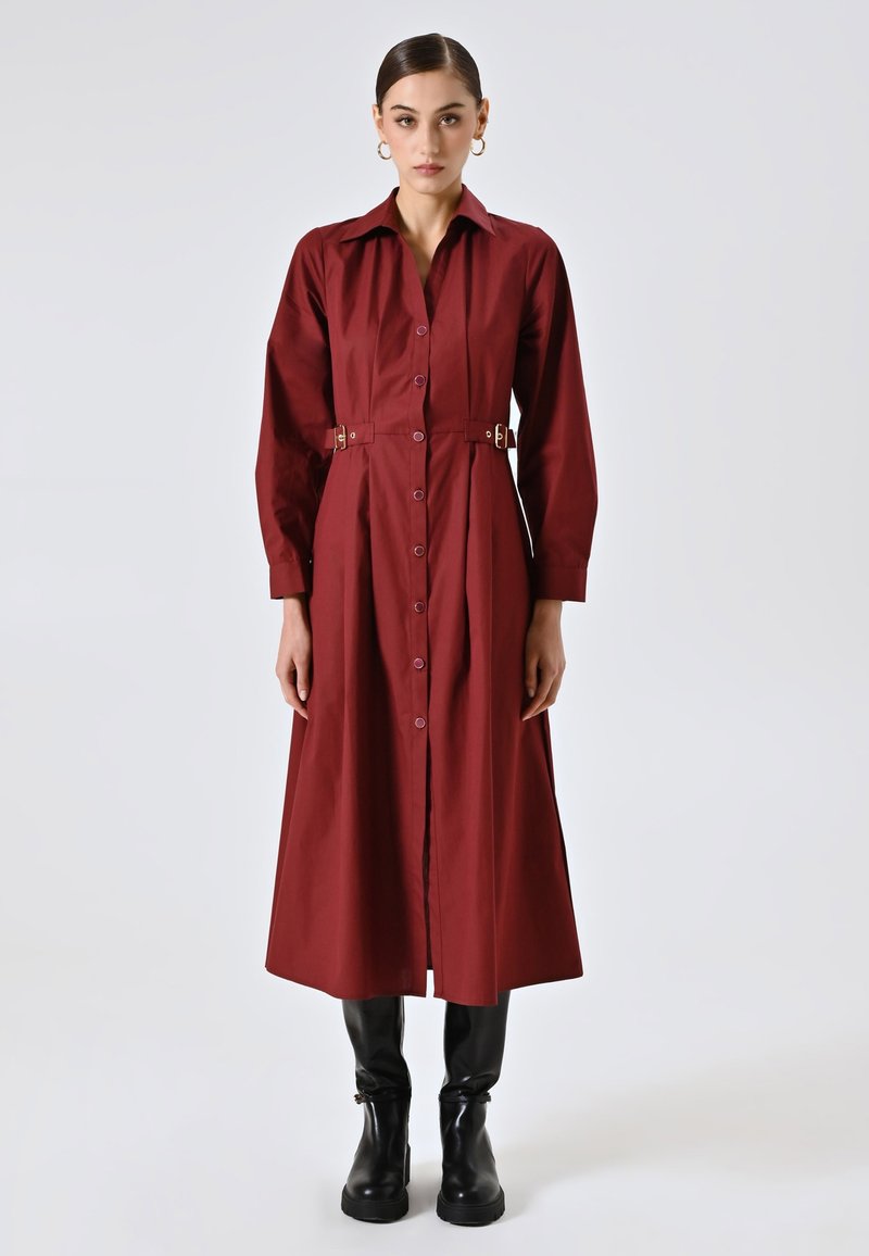 Abito button-up bordeaux con maniche lunghe, colletto, dettagli con cintura laterale e gonna svasata, abbinato a stivali neri alti fino al ginocchio.