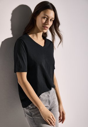 T-shirt noir en coton à col en V avec manches courtes, associé à un jean gris clair. Texture de tissu douce, coupe décontractée, sans motifs ni accents visibles.
