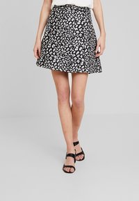 Jupe noire à motif animalier blanc, coupe évasée, tissu lisse et taille unie, associée à des sandales noires à lanières.