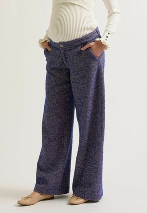 Pantalon large en tissu bleu en chevron texturé, doté de poches avant et d'une fermeture à bouton, associé à des chaussures plates beiges.