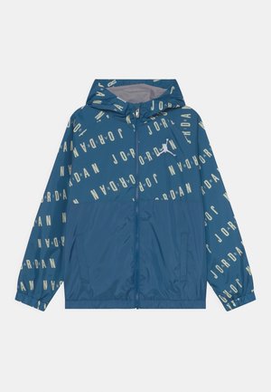 Blaue Kapuzenjacke mit durchgehendem Reißverschluss, verstreutem "JORDAN"-Schriftzug und weißem Jumpman-Logo auf der Brust, ausgestattet mit elastischen Bündchen und Seitentaschen.
