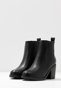 Czarne botki za kostkę wykonane z gładkiej skóry, z prążkowanymi bocznymi panelami, zaokrąglonym noskiem i słupkowym obcasem. Posiadają uchwyt z tyłu dla łatwego zakupu.