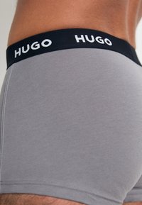 Boxer brevissimi in cotone grigio con vita elastica nera, caratterizzati dal logo bianco "HUGO". Texture liscia e design aderente per il massimo comfort.