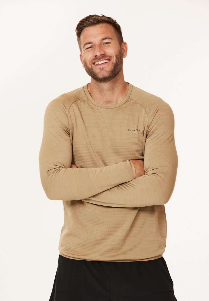 Beige langærmet skjorte med tekstureret overflade og rund halsudskæring, der har et diskret logo på brystet. Enkel, atletisk pasform.
