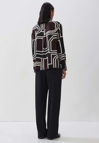 Long-sleeve shirt in black and white geometric pattern, featuring a relaxed fit, smooth fabric, and buttoned cuffs, paired with black trousers.