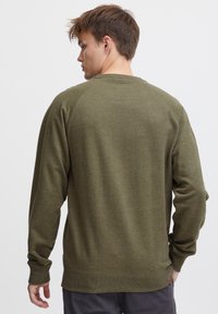 Hanorac verde măsliniu cu manșete și tiv ribbate, material texturat și mâneci raglan. Vederea din spate arată o branding minim la baza hanoracului.