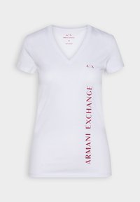 Camiseta blanca de algodón con cuello en V, que presenta el texto en rojo oscuro "ARMANI EXCHANGE" verticalmente en el lado izquierdo y un logotipo en el pecho.
