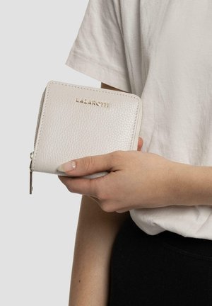 Portefeuille en cuir blanc avec une finition texturée, logo doré en relief, fermeture zippée et design minimaliste, tenu dans une main.