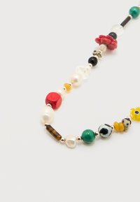 Κολιέ με πολύχρωμες χάντρες που περιλαμβάνει μαργαριτ άρια, πράσινες, κόκκινες, κίτρινες, μαύρες και χάντρες με σχέδιο σε λευκό φόντο.