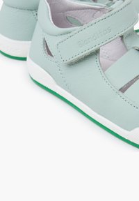 Sandalias de cuero verde claro con suelas de goma blanca y verde, que cuentan con una correa de gancho y bucle y detalles recortados en los lados para mayor transpirabilidad.
