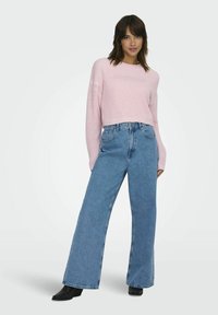 Maglione cropped lavorato a maglia di un rosa chiaro abbinato a jeans a gamba larga blu. Stivali neri alla caviglia completano l'outfit. Stile semplice e moderno.