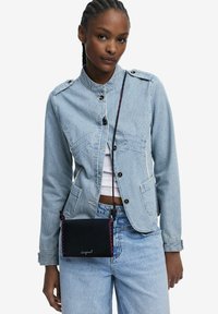 Gestreifte Jeansjacke in Hellblau mit Knopfverschluss, kombiniert mit blauen Jeans und einer kleinen schwarzen Umhängetasche mit rosa Nähakzenten.