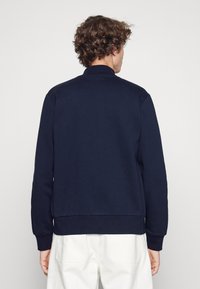 Sweatshirt bleu marine, texture douce, col montant, poignets et ourlet côtelés, montré de dos avec un design uni.