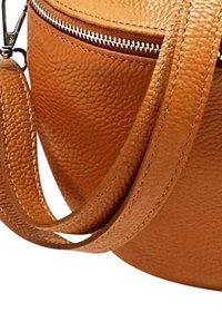 Ronde lederen tas in een rijke tan kleur, met een gestructureerde oppervlakte, voorzien van een zilveren rits en een brede schouderband. Close-up die details en stiksels toont.