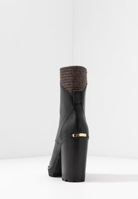 Stivale alla caviglia in pelle nera con una parte superiore in brown texturizzato, tacco spesso e dettagli in oro. Presenta una finitura liscia e una silhouette moderna.